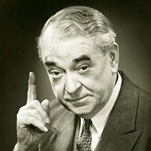 Senior man raising index finger in studio, (B&W), close-up, portrait