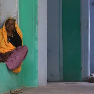 Senior woman sitting in front door of home, smiling, portrait