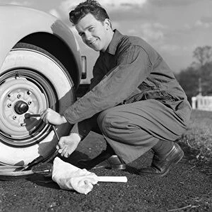Smiling man in coveralls using tire iron to change tire on sedan