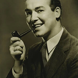 Smiling man with pipe in mouth posing in studio, (B&W), close-up, portrait