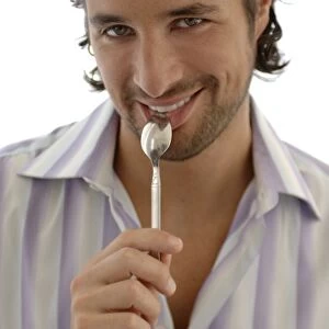 Smiling man with a spoon in the mouth, snacking