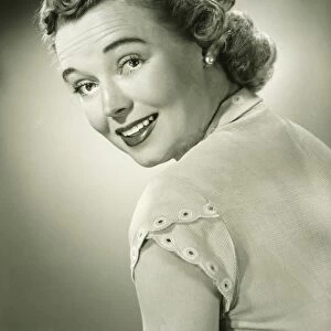 Smiling woman looking over shoulder in studio, (B&W), portrait
