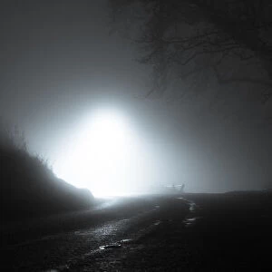 A spooky, eerie country road passing through a hill. With a light in the distance