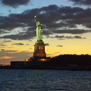 Statue of Liberty illuminated at sunset with dramatic sky, New York City, USA