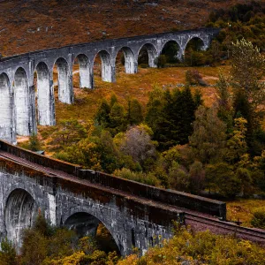 Steam train crossing the Glenfinnan bridge with autumn colors in Scotland