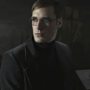 Student wearing a suit and glasses, sitting in front of a painting