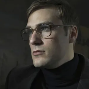 Student wearing a suit and glasses, sitting in front of a painting