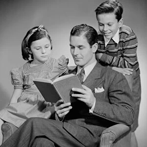 Studio shot of father with two children (10-11) reading book