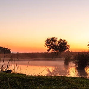 The sun rises over a small dam in the high veld winter landscape near Hartebeespoort, South Africa