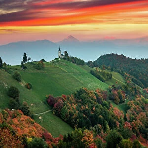 Sunset landscape of church Jamnik in Slovenia on green hill with mountains background
