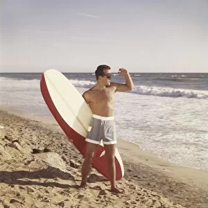 Surfer holding surfboard on beach