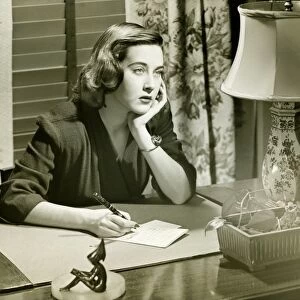 Thoughtful woman writing letter at desk, (B&W)