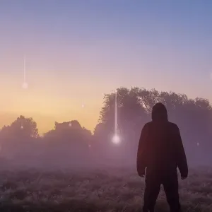A UFO, supernatural concept. A hooded figure with his back to the camera A UFO, supernatural concept. A hooded figure with his back to the camera