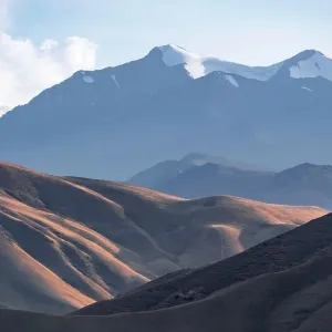 View over eroded mountainous landscape with brown hills, high mountains with snow in the back, Konorchek Canyon, Chuy, Kyrgyzstan View over eroded mountainous landscape with brown hills, high mountains with snow in the back, Konorchek Canyon, Chuy, Kyrgyzstan