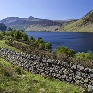 View over an old English stone wall towards the blue lake of Crummock Water, Lake District National Park, Cumbria, England, United Kingdom