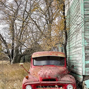 A vintage red pick-up truck parked beside an abandoned house