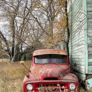 A vintage red pick-up truck parked beside an abandoned house