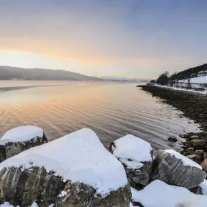 Winter atmosphere at sunrise on the fjord, snow-covered rocks, coastal road, near Alesund, Norway