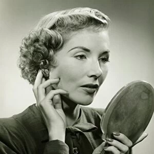 Woman adjusting earring, holding hand mirror, (B&W), portrait