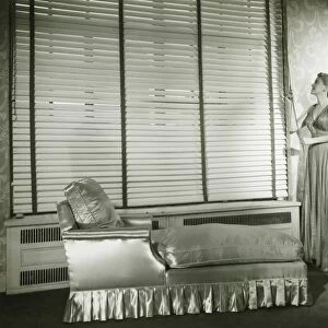 Woman adjusting window blind in living room, (B&W)