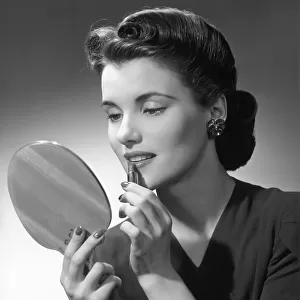 Woman applying lip-stick looking in hand-held mirror