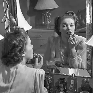 Woman applying lip-stick in front of mirror