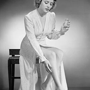 Woman applying perfume on leg, (B&W), portrait