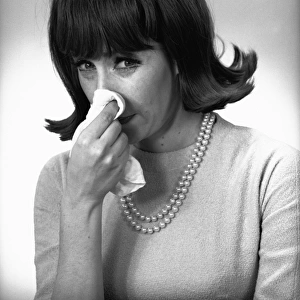 Woman blowing nose in studio, (B&W)