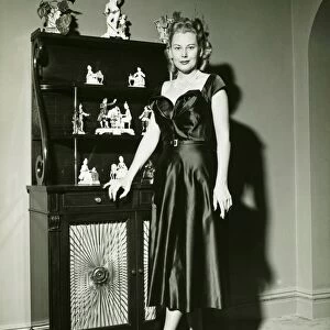 Woman in evening gown posing at cabinet, (B&W), (Portrait)