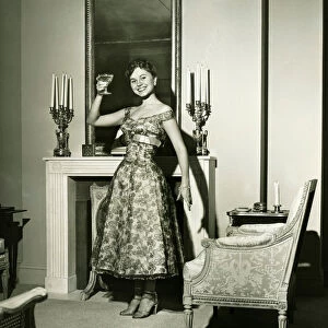 Woman in evening gown toasting by fireplace, (B&W), portrait