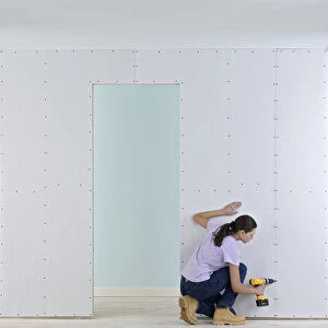 Woman holding screwdriver to wall of plasterboard
