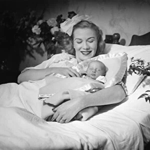 Woman lying on bed, holding new born baby (B&W)