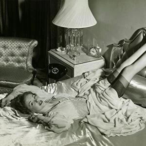 Woman lying on bed with legs on backrest, (B&W), elevated view