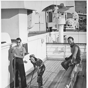 Woman and two men on cruiser deck, (B&W), elevated view