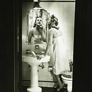 Woman removing make up in front of mirror in bathroom, (B&W)