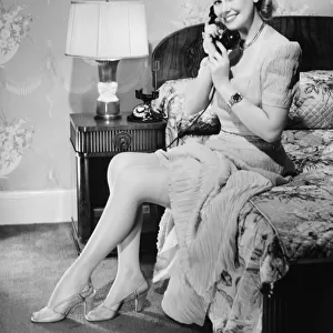 Woman sitting on bed, talking on phone, (B&W)
