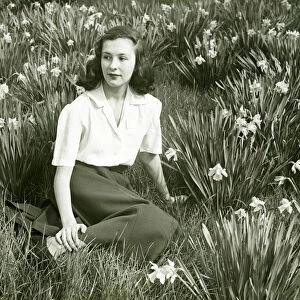 Woman sitting on grass among blooming daffodils, (B&W), (Portrait)