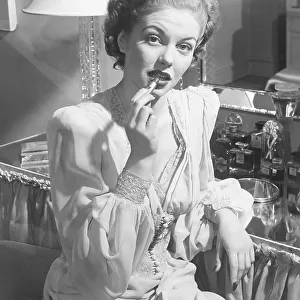 Woman sitting at vanity table, putting on lipstick, (B&W), portrait