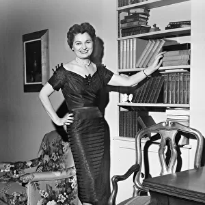 Woman standing in rich living room with hand on shelf, (B&W)