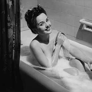 Woman taking bubble bath, holding soap bar, (B&W), portrait