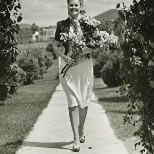Woman walking on path, holding bunch of field flowers, (B&W)