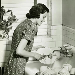 Woman washing dishes at kitchen sink, (B&W)