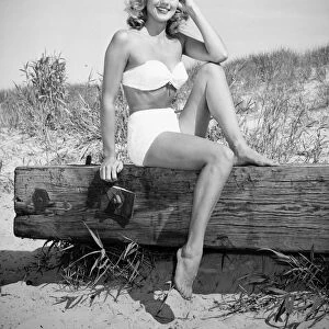 Woman wearing bikini sitting on log on beach, (B&W), (Portrait)