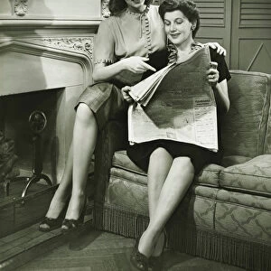 Two women sitting by fireplace, reading newspaper, (B&W)