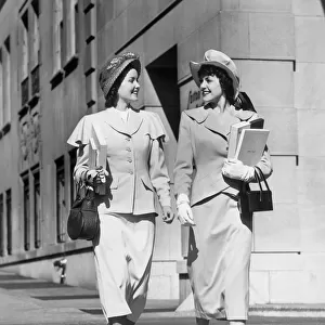 Two women walking along sidewalk in city
