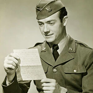 World War II Army solider reading letter in studio, (B&W), portrait