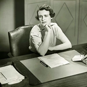 Worrying woman sitting at desk in office, (B&W)