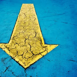 Yellow arrow on blue concrete with cracks