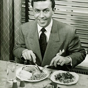 Young businessman eating dinner, (B&W), portrait