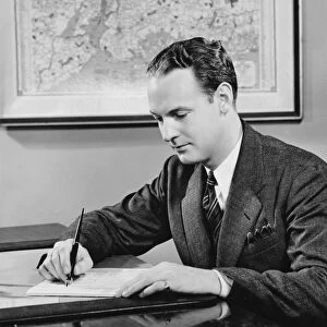 Young businessman sitting at desk, writing, (B&W)